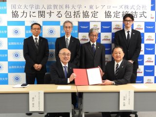 遠山学長（前列左）、矢島代表取締役社長（前列右）、黒澤理事・副学長（後列左）、野﨑理事・副学長・病院長（後列左２番目）、相見理事・副学長（後列左３番目）、高杉事務局長（後列右）による記念撮影